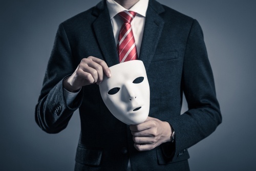 man in business suit holding a mask to illustrate impersonation of a public servant