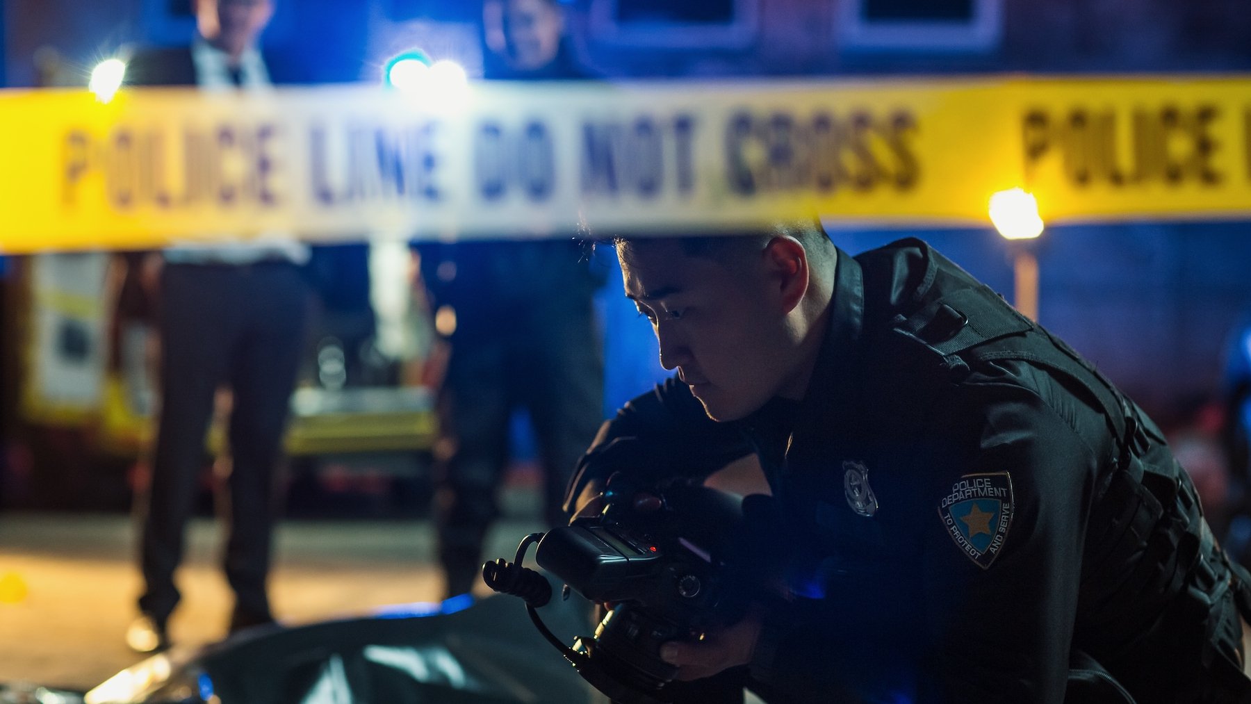 Police officer outside investigating a crime behind yellow "police line do not cross" tape