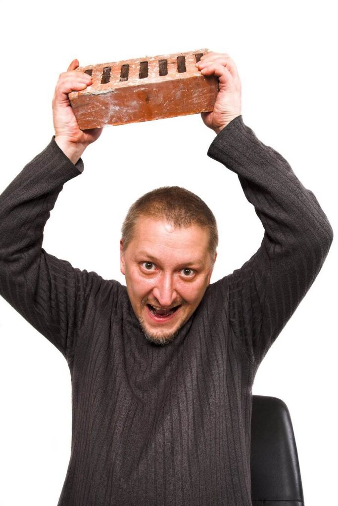 Man in grey sweater menacing by holding a brick in a throwing position against a white background