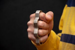 Man's fist wearing brass knuckles (which is illegal in Colorado) against a black background
