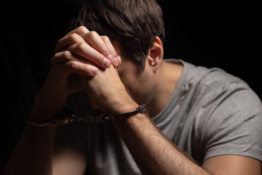 Man in handcuffs holding his head in his hands following an arrest for wholesale promotion of obscenity