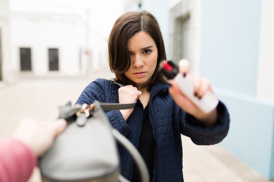 Woman dispensing pepper spray at a thief who is grabbing her pocketbook 