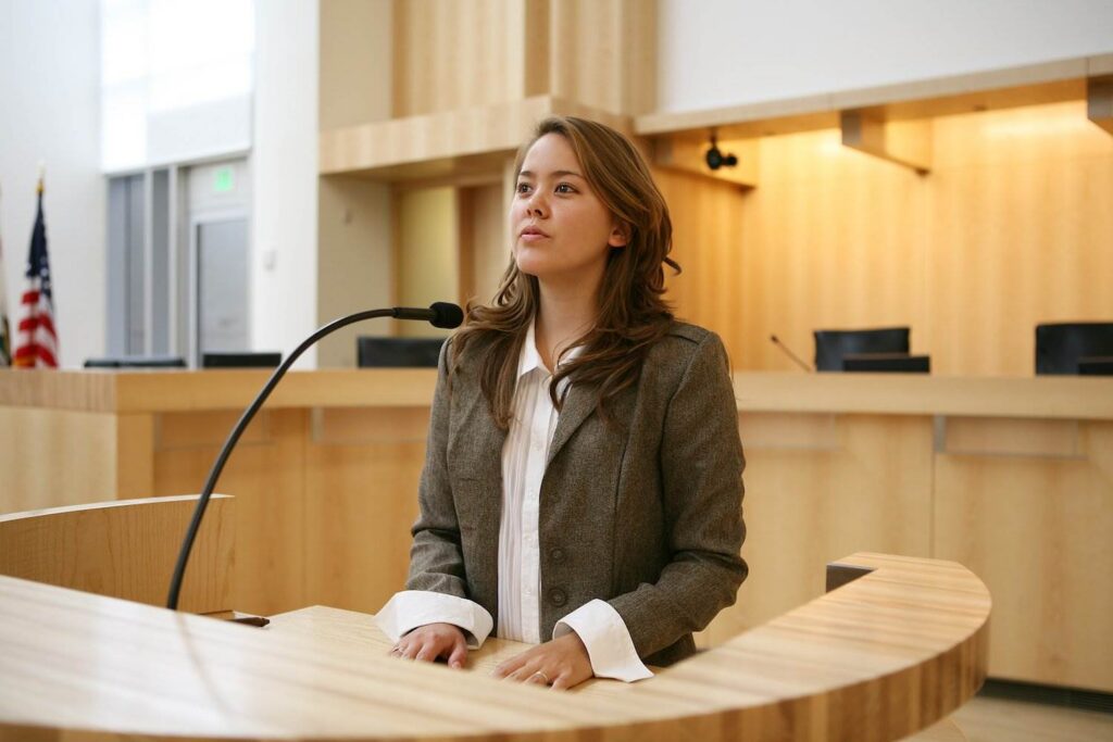 Woman on witness stand in a wooden courtroom about to commit perjury