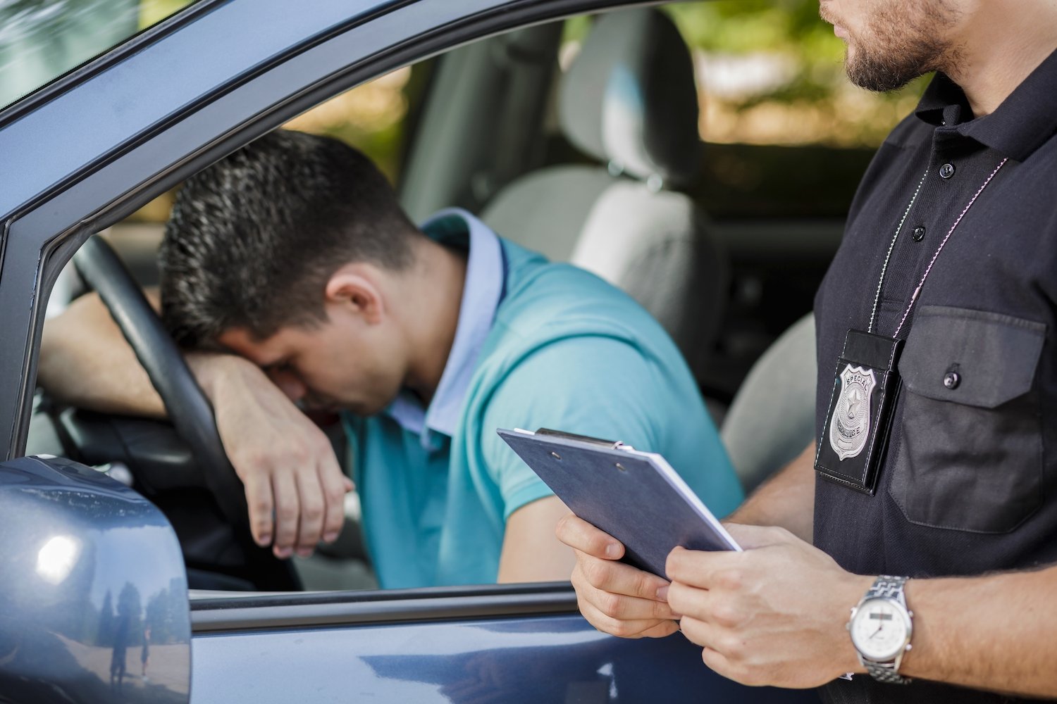 Male driver leaning on his steering wheel during a traffic stop while a police officer issues him a ticket