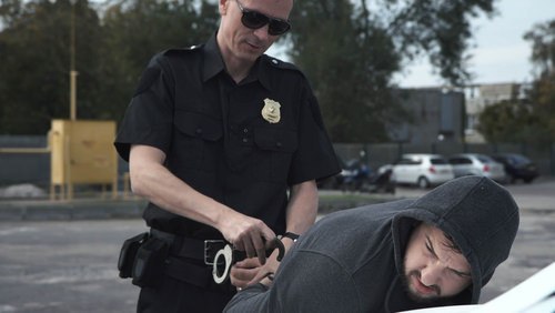 Officer in a parking lot handcuffing a suspect in a hoodie, though the officer is not reading him his Miranda rights since the suspect is not being interrogated