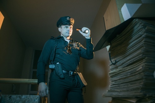 Police officer holding a flashlight conducting a search in a room with several papers piled around