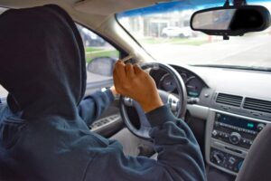 Man in a hoodie holding a joint in one hand while steering his car with another in violation of Colorado's DUI of marijuana laws. 