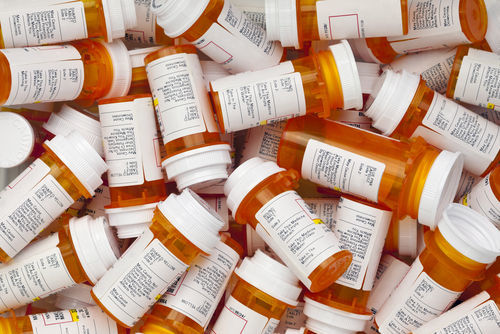 Bird's eye view of a large pile of dozens of orange prescription pill bottles with white caps and labels