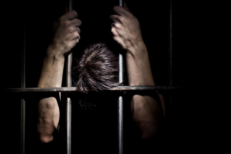 Prison inmate clasping onto cell bars in despair