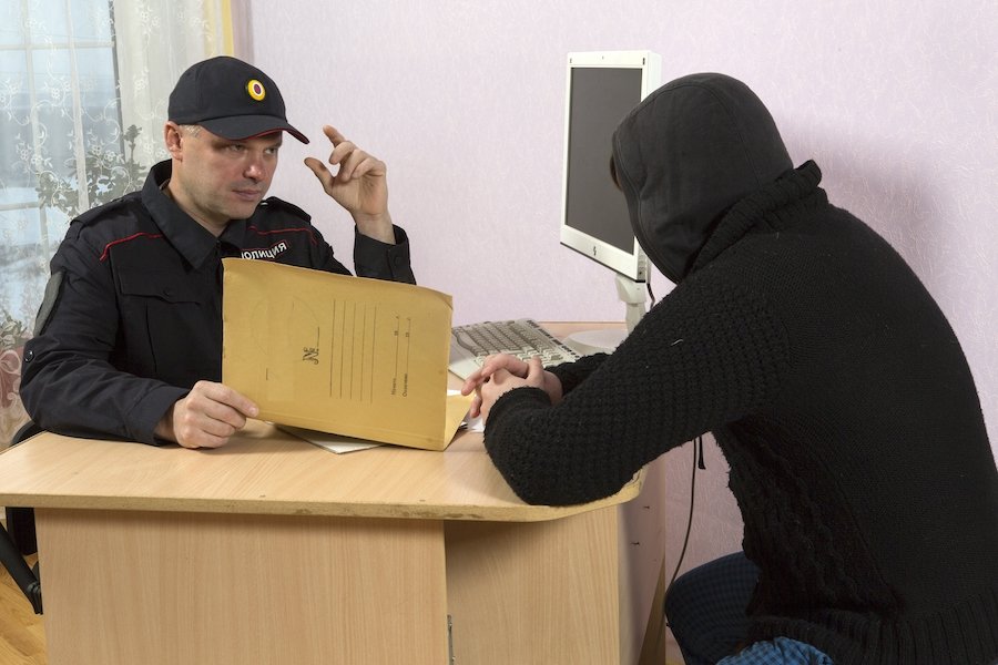 Probationer in a hoodie checking in with a probation officer at his desk, and the PO is holding a file