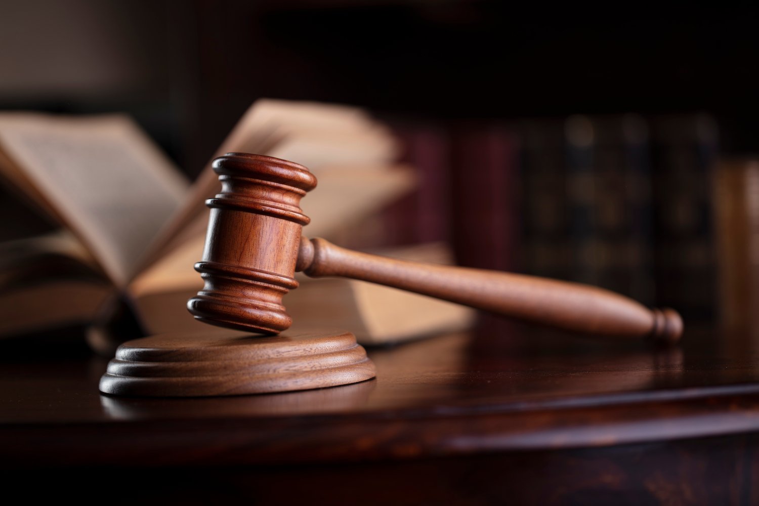 Judge's gavel and an open law book on a desk with a bookshelf of law books in the background