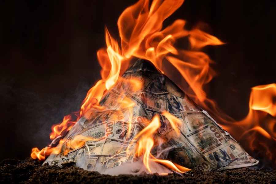 A pyramid of money set aflame to illustrate how pyramid schemes are set up to fail. 
