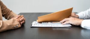 Closeup of two people at a table sneaking money in an envelope, suggesting fraudulent activity
