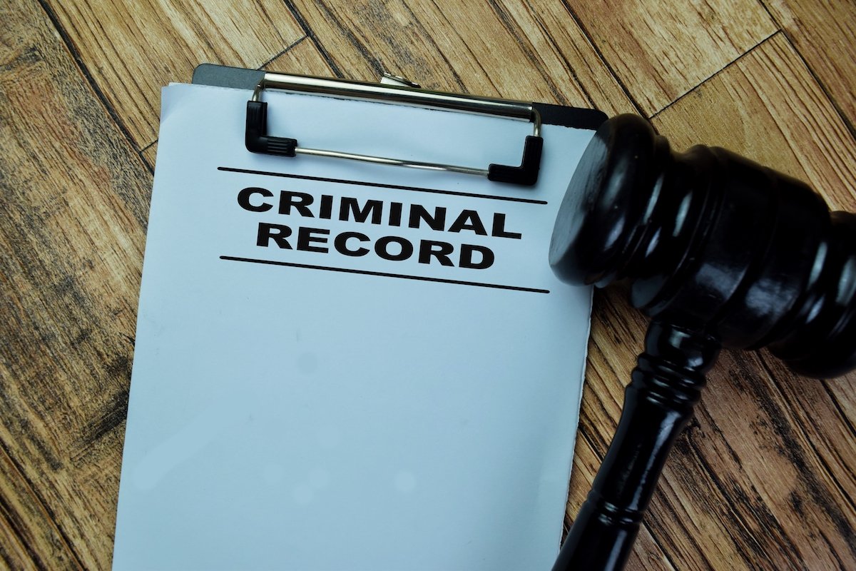 Clipboard holding a paper that says "Criminal Record" next to a judge's gavel on a wooden table