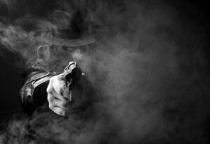 Mobster in black trench coat obscured by cigarette smoke against a black background