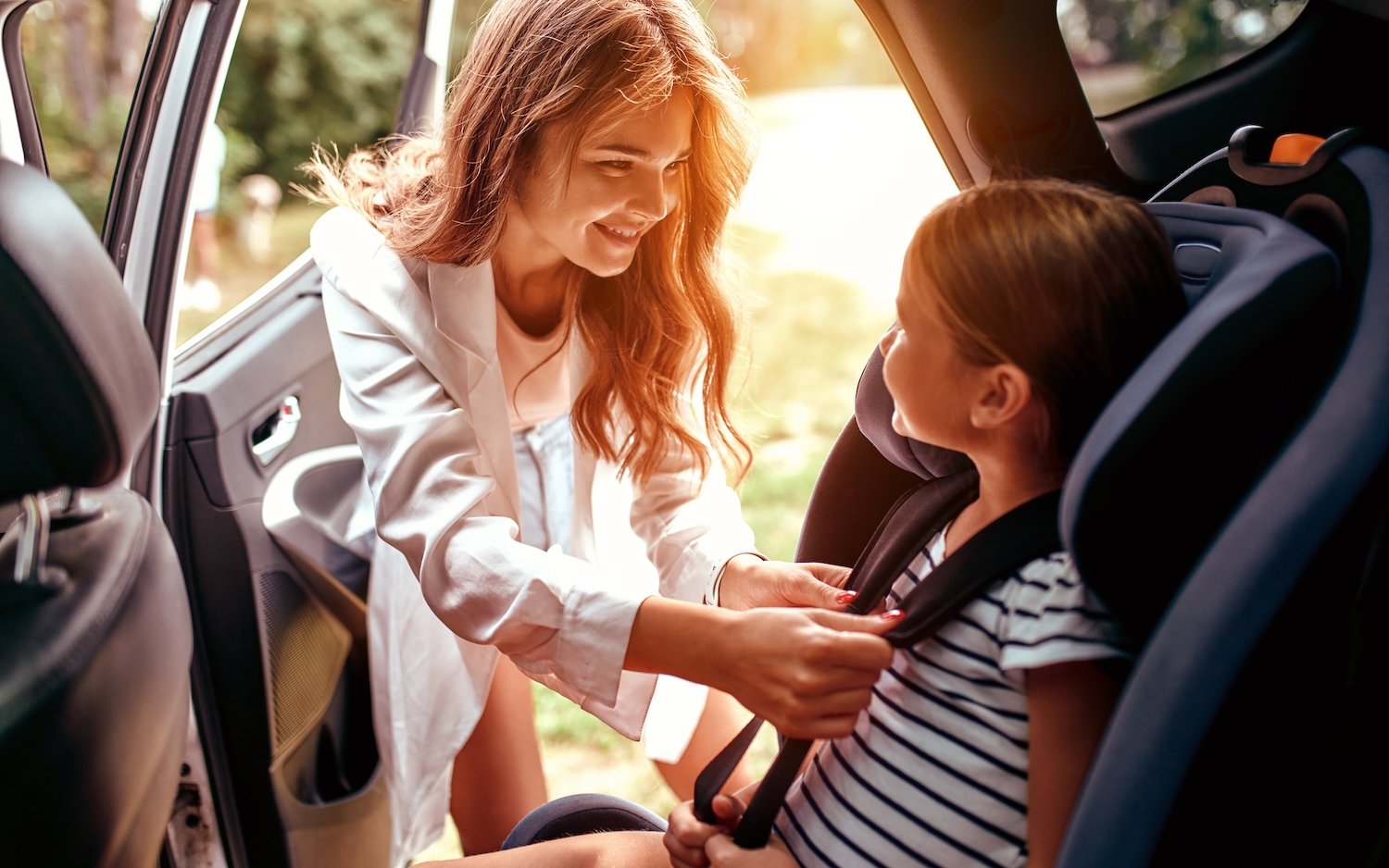 Mother fastening her daughter into a car seat in the back seat