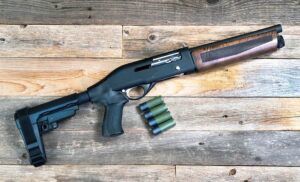Home security 12 gauge short barrel semi- auto firearm/ shotgun resting on a wooden plank floor with four bullets.