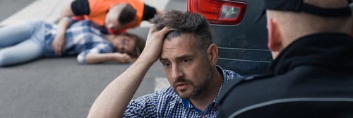 Driver holding his head following a DUI resulting in a car accident with a victim lying on the street