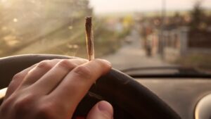 Closeup of a hand holding a joint while on a steering wheel in violation of Colorado's DUI of marijuana laws