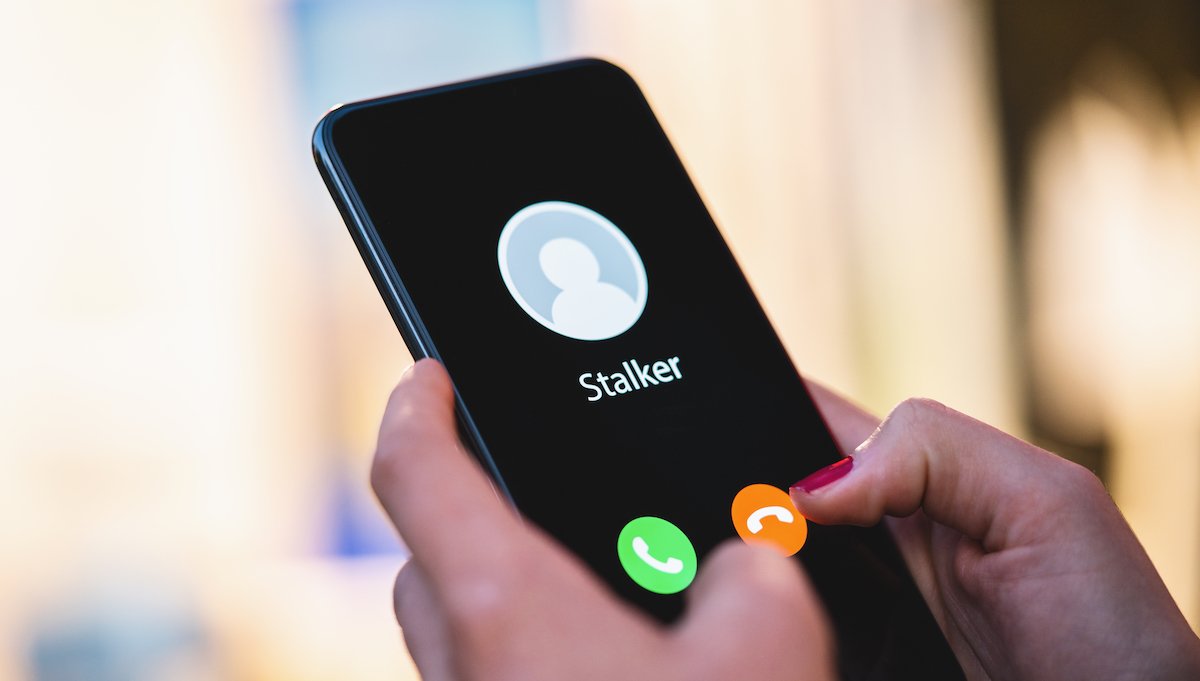Woman holding a phone with an incoming call from a contact called "Stalker"