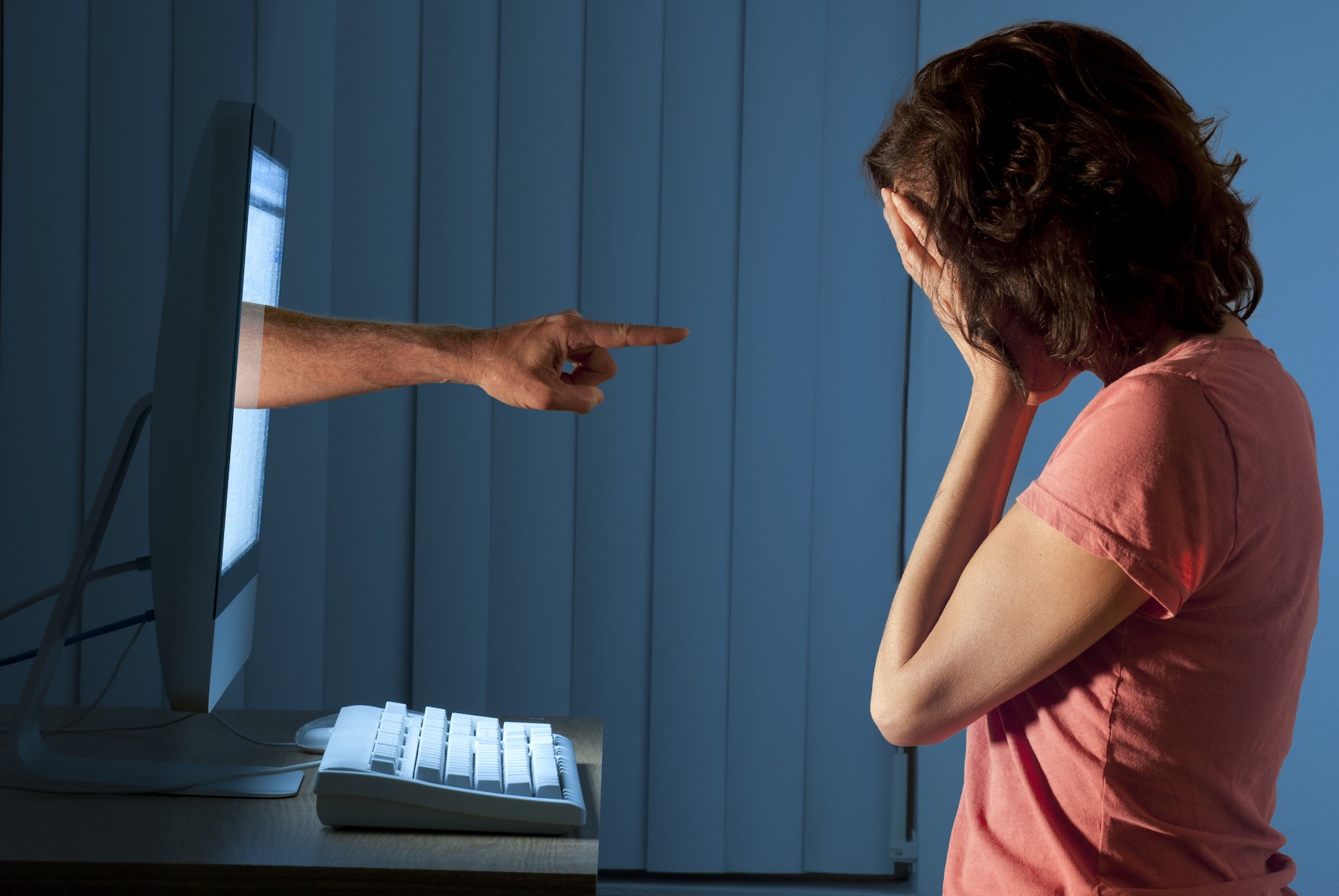 Stalking victim holding her head in her hands as a stalker's hand bursts through her computer screen