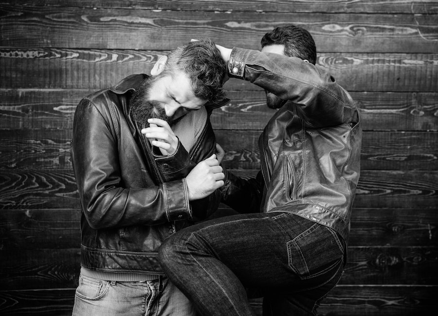 Black and white photo of two men in leather jackets and denim jeans in a fist fight against a wooden wall