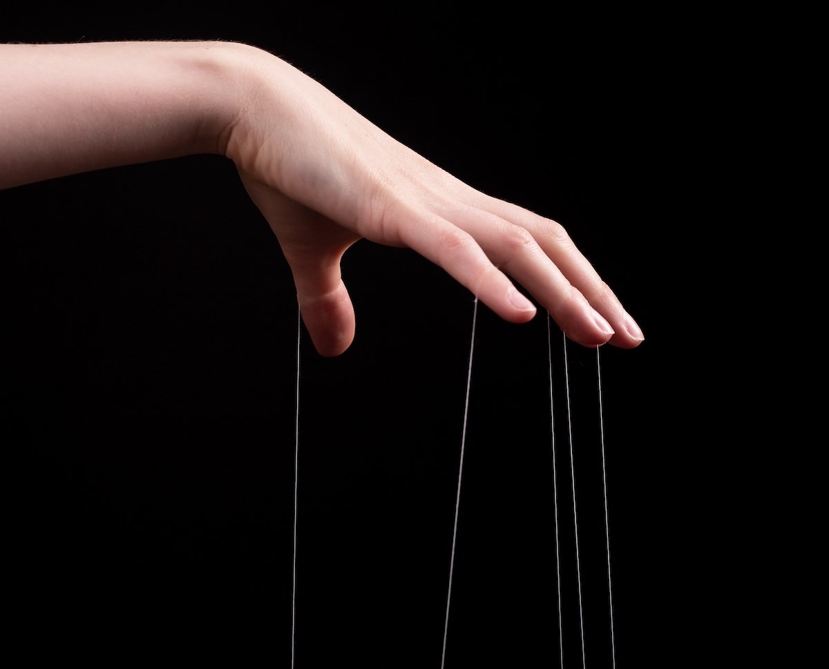 Man's hand holding puppet strings against a black background