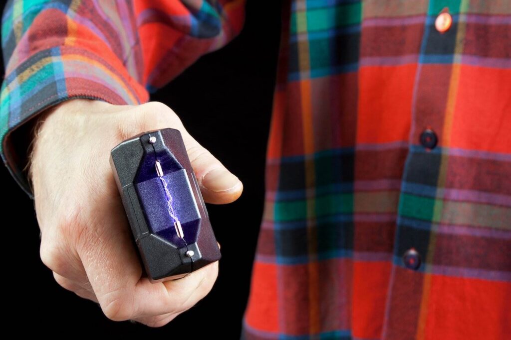 Man in plaid shirt holding out stun gun in lawful act of self-defense against an aggressor