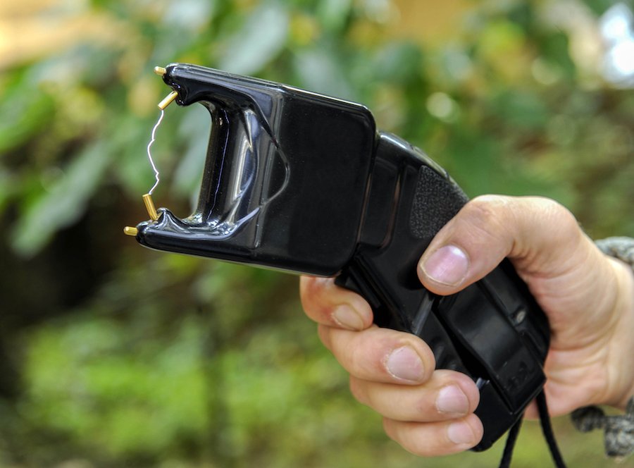 Closeup of hand holding out and deploying a stun gun against a foliage background