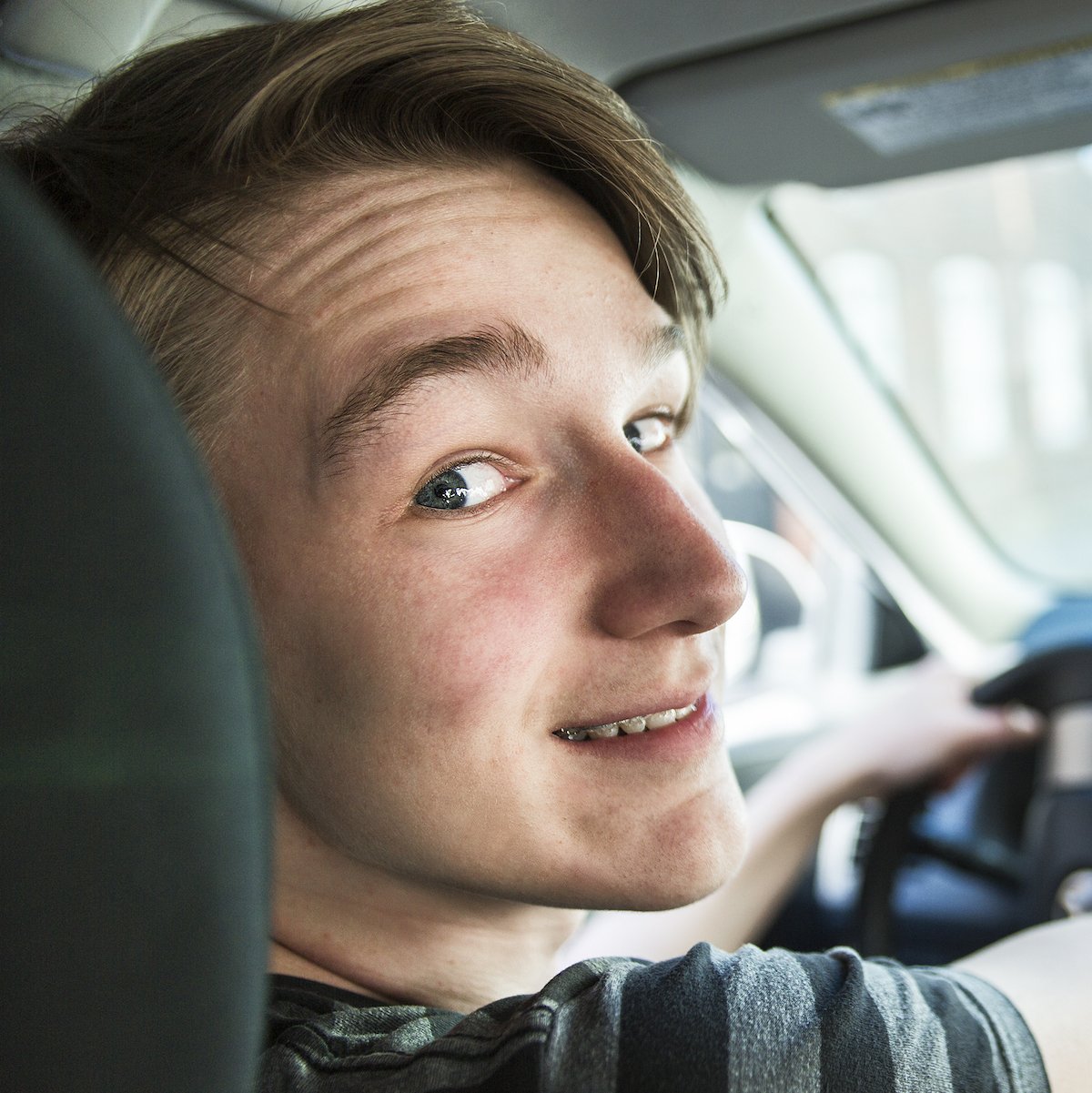 Teen driver looking backwards and smiling at the camera