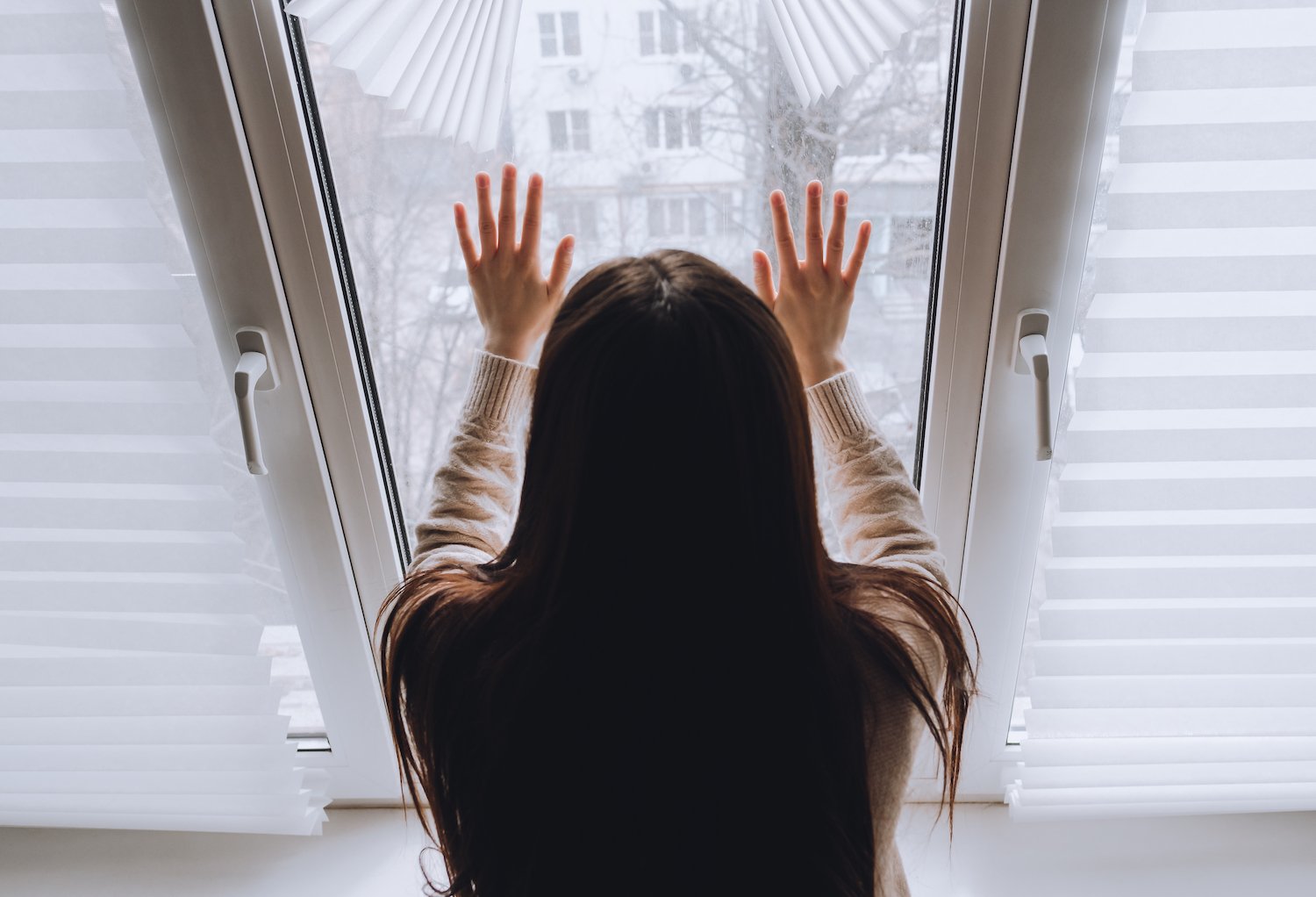 Woman on house arrest holding the window pane and staring outside