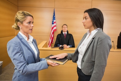 Witness being sworn in before a trial with a judge looking on